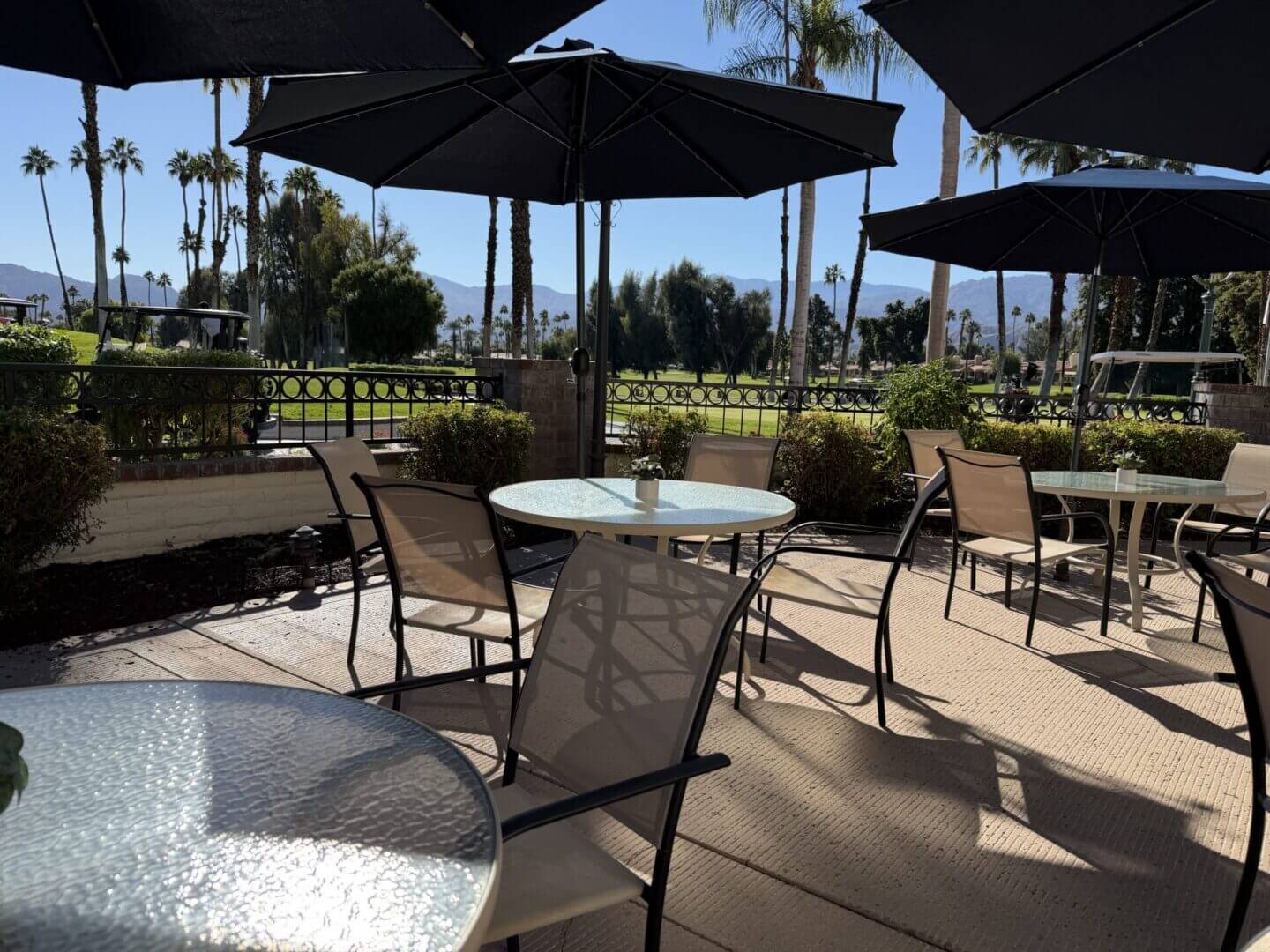 Outdoor patio seating with round tables and umbrellas on a sunny day.