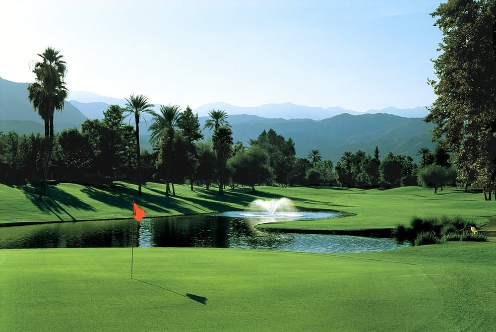 A serene golf course with a water hazard and distant mountains.