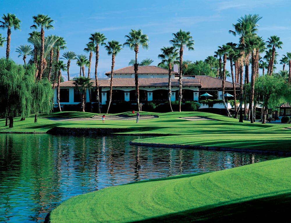Golf course with palm trees and water hazard under a clear blue sky.